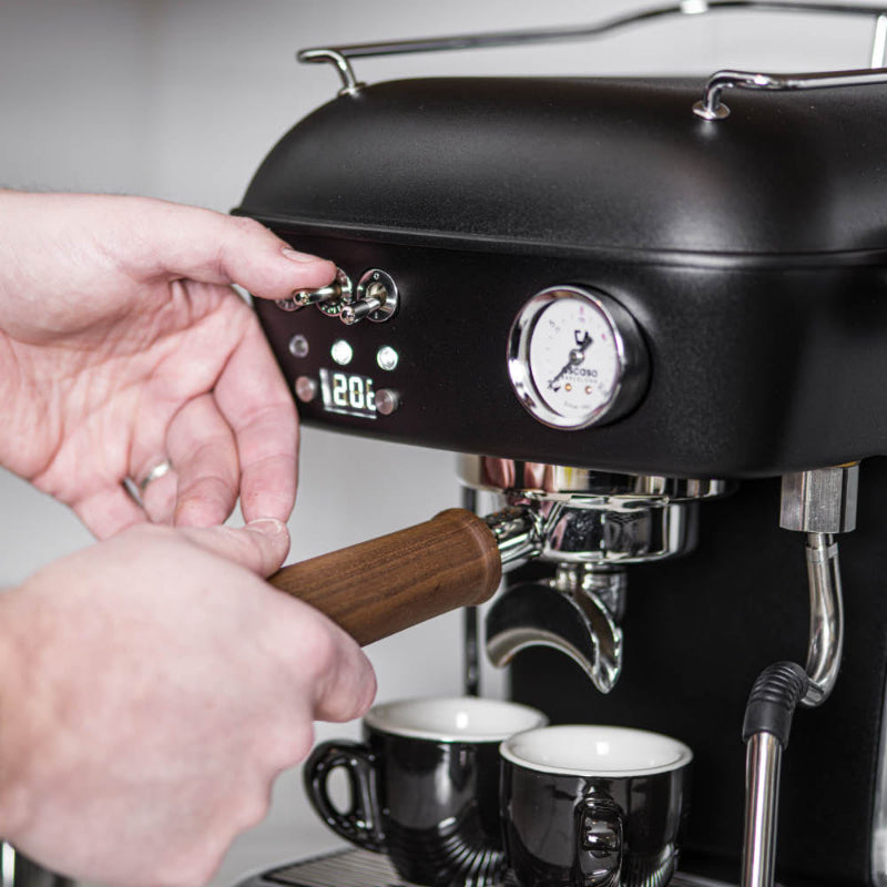 Person using an espresso machine with two cups on a light background