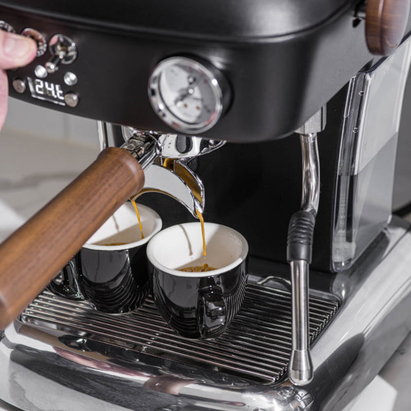 Espresso machine dispensing coffee into two cups with a person's hand adjusting the machine.